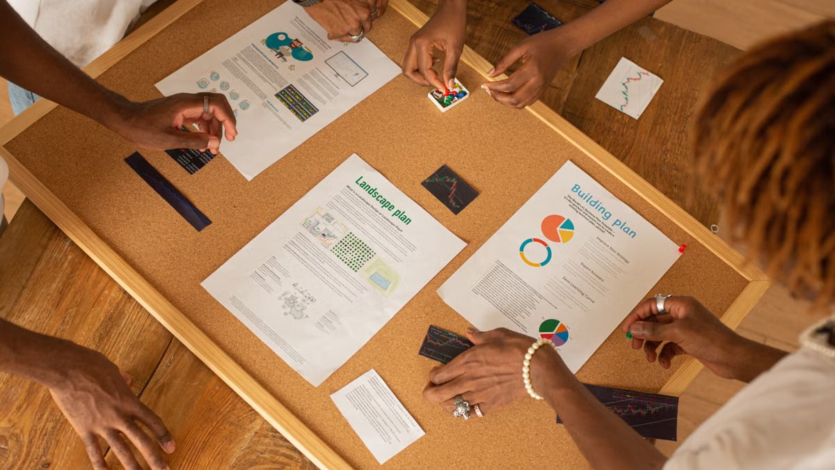 A diverse team collaborates on a workspace board with charts and plans.